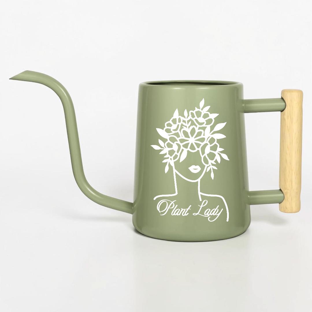 Sage green watering can with a long, slender spout and a wooden handle. The can features a white graphic of a woman's face with a floral crown and the words "Plant Lady".