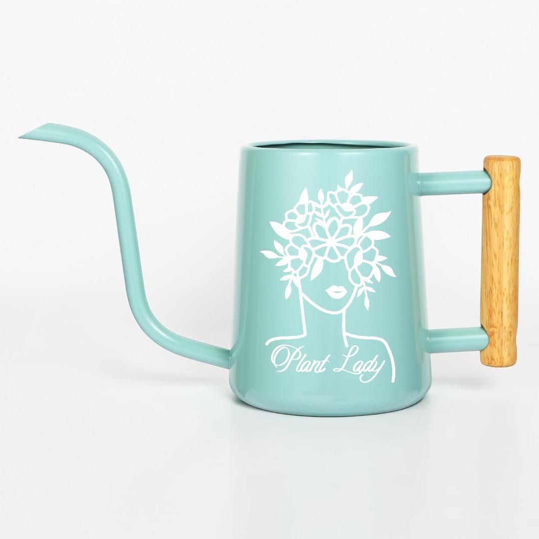 A teal watering can with a long, curved spout and a wooden handle. The can features a white graphic of a woman's face with a floral crown and the words "Plant Lady".