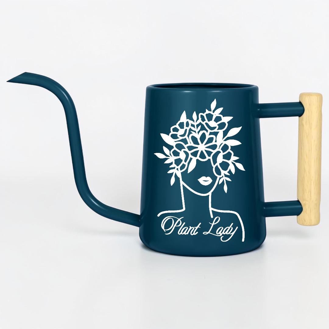 A dark blue watering can with a long, curved spout and a wooden handle. The can features a white graphic of a woman's face with a floral crown and the text "Plant Lady".