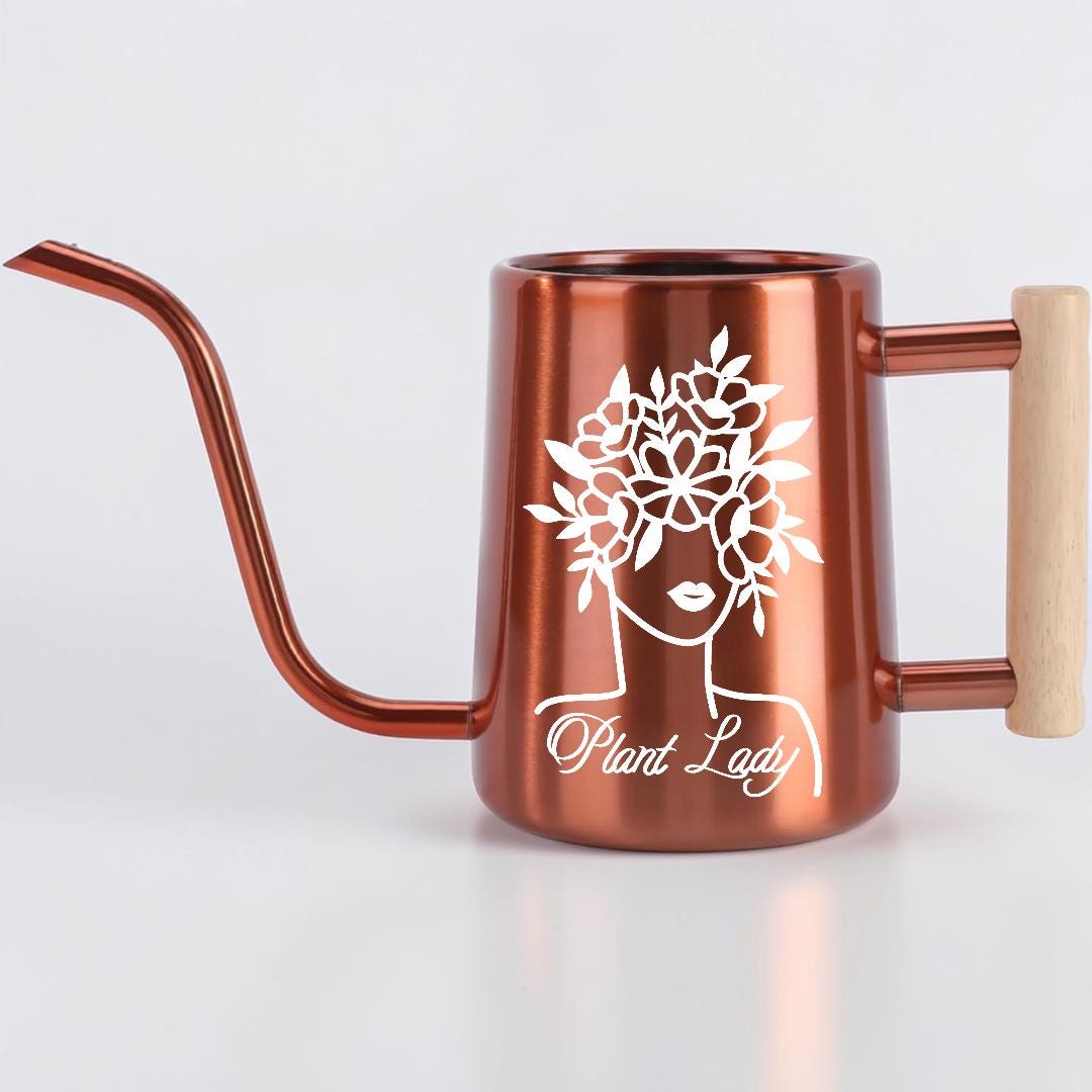 Copper-colored watering can with a long spout and wooden handle. The can features a white graphic of a woman's face with a floral crown and the words "Plant Lady" in a script font. Ideal for indoor or outdoor plant care.