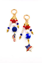 Two keychains with patriotic themes. Each keychain features gold-colored hardware, red, white, and blue beads, and star-shaped charms. One has a flip-flop charm with the American flag, the other has a star charm with the American flag.