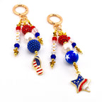 Two keychains with patriotic themes. Each keychain features gold-colored hardware, red, white, and blue beads, and star charms. One has a flip-flop charm with the American flag, and the other has a star charm with the American flag.