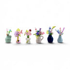 A collection of six miniature vases, each containing a unique arrangement of colorful glass beads, faux flowers, and decorative accents. The vases vary in shape, size, and color, including shades of light blue, pink, clear, and dark blue.