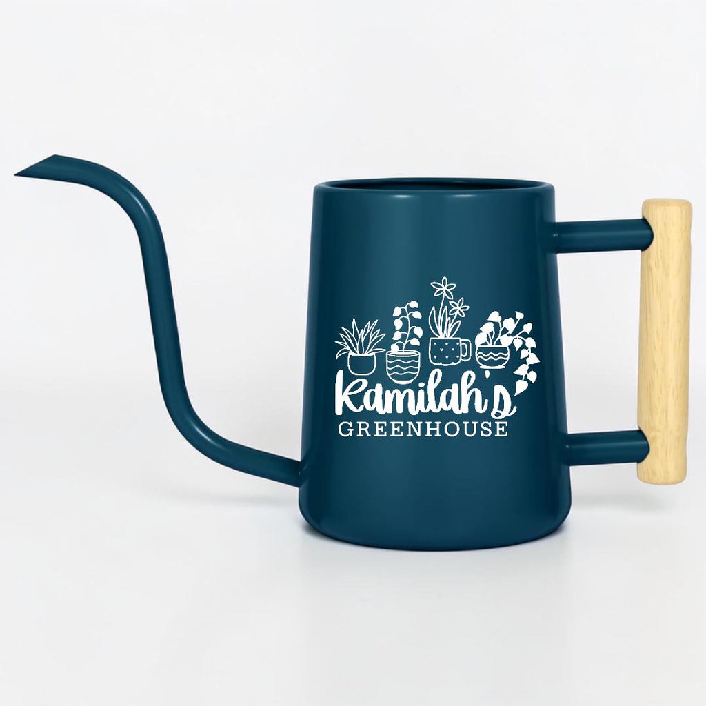 A dark blue metal watering can with a long, slender spout and a light-colored wooden handle. The side features a white graphic of four potted plants above the text "Kamilah's GREENHOUSE" in a mix of script and block lettering.