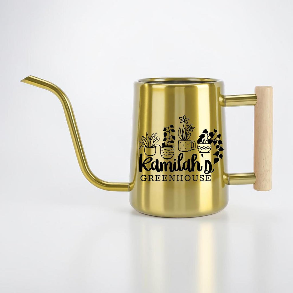 A gold-colored stainless steel watering can with a long, slender spout and a light-colored wooden handle. The side of the can features a black graphic of four potted plants and the text Kamilah's GREENHOUSE printed in black.
