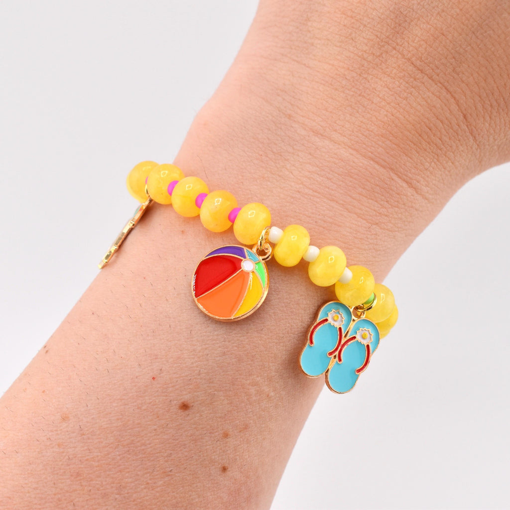 A beaded bracelet featuring yellow round beads with small pink and white spacers. The bracelet includes two metal charms: a round, multi-colored beach ball charm and a pair of light blue flip-flop sandals with red straps.