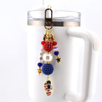 A patriotic keychain charm with red, white, and blue beads, gold stars, and a flip-flop charm featuring the American flag. The charm is attached to a bronze-colored clasp and is hanging on a white mug.