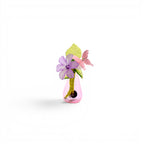 A small pink glass teardrop vase containing a purple flower, a light green leaf, and a pink butterfly figurine. The stems are visible inside the translucent pink glass, and the arrangement is accented with small white beads.