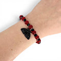 A beaded bracelet featuring alternating smooth red spherical beads and smaller faceted black beads. A black moth-shaped charm hangs from the center of the bracelet. The beads are strung on an elastic cord, creating a circular design.