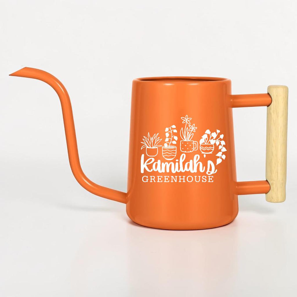 An orange metal watering can with a long, thin spout and a light-colored wooden handle. The side features a white graphic of four potted plants and the text Kamilah's GREENHOUSE printed in a stylized font on the front surface.