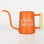 An orange metal watering can with a long, thin spout and a light-colored wooden handle. The side features a white line-art graphic of five potted plants above the text Custom Text and OPTIONAL LINE 2 in a white script font.