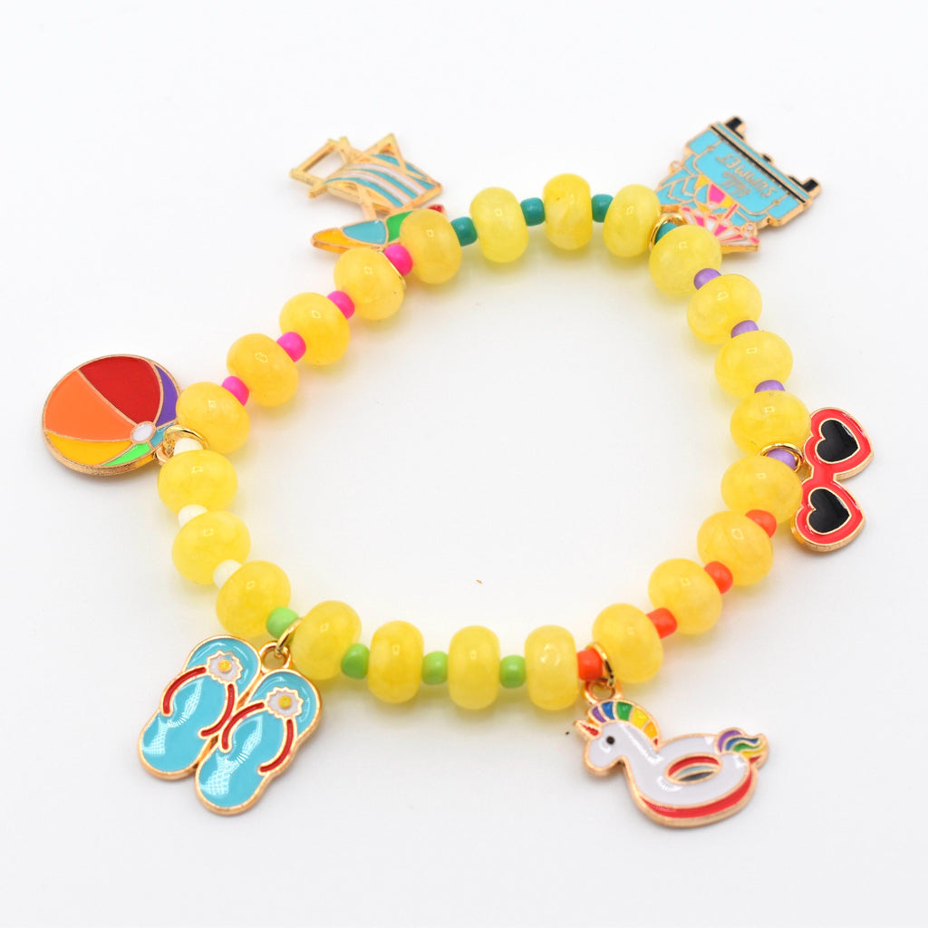 A stretch bracelet featuring translucent yellow round beads separated by small colorful spacer beads. The bracelet includes several metal charms: a beach ball, blue flip-flops, a unicorn pool float, heart-shaped sunglasses, and a beach chair.