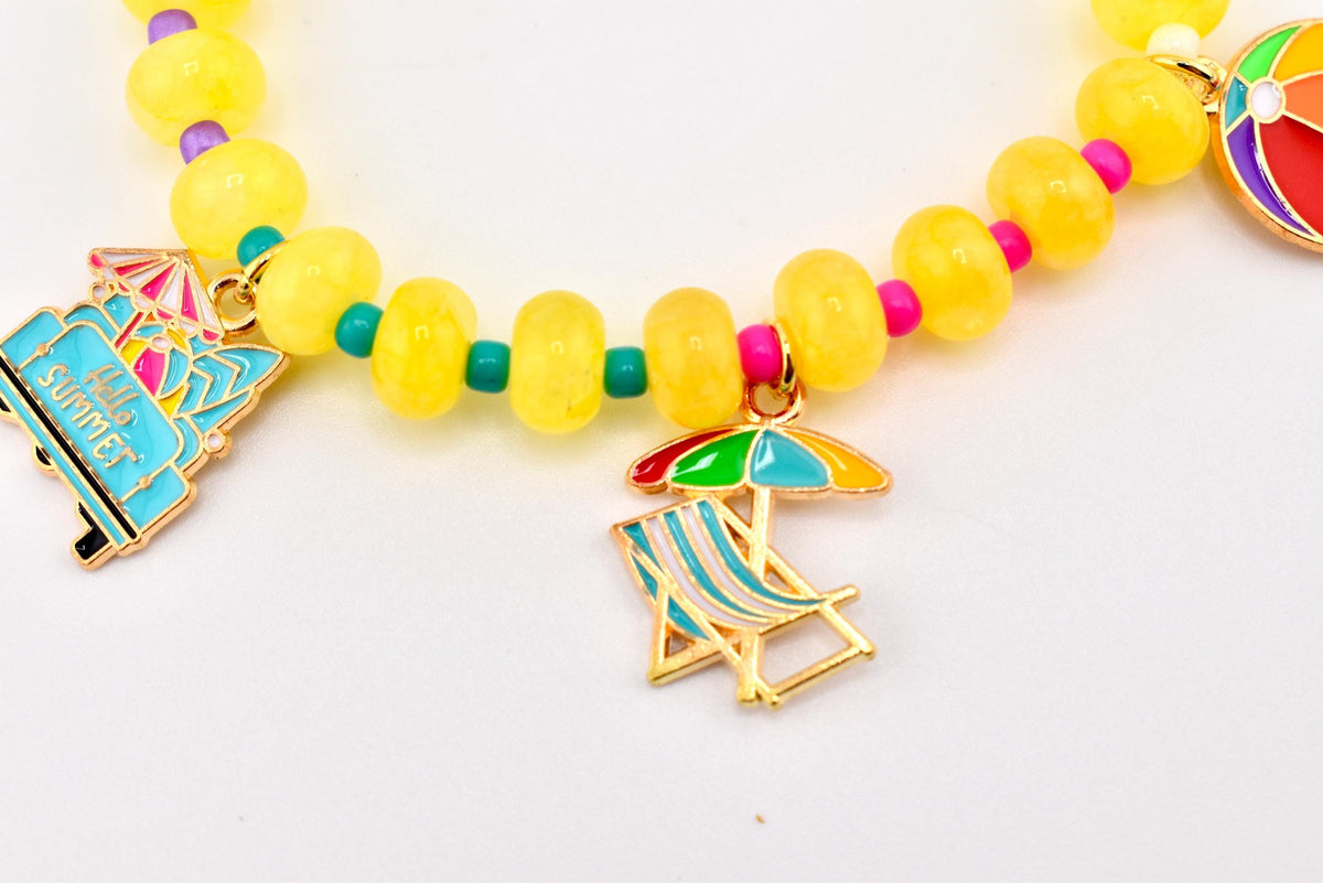 A beaded bracelet featuring translucent yellow round beads separated by small teal and pink spacer beads. The bracelet includes gold-tone metal charms: a blue van with the text Hello SUMMER, a beach chair with an umbrella, and a beach ball.