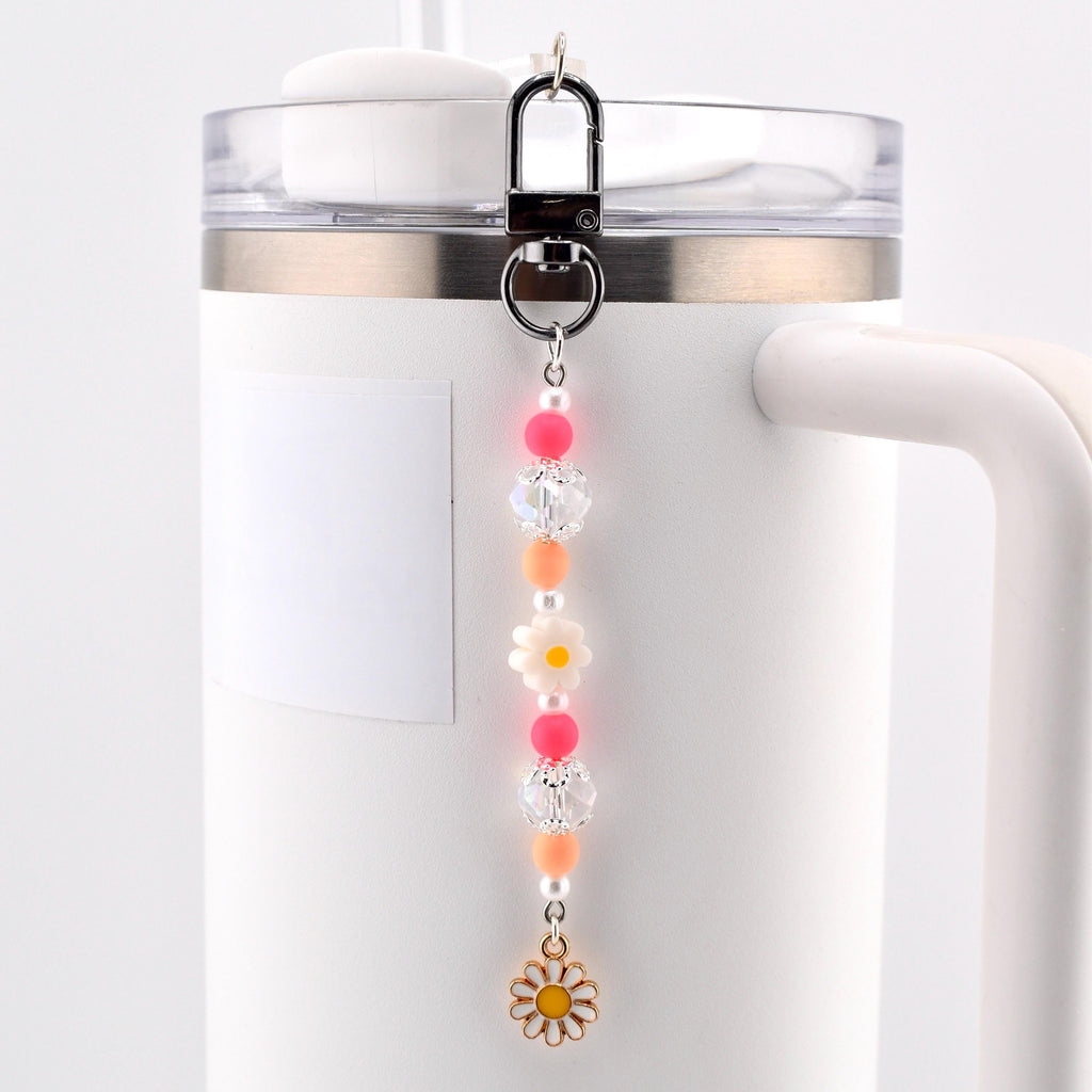 A beaded charm accessory featuring a silver-toned lobster clasp, pink and orange spherical beads, clear faceted beads, small white pearls, a white flower-shaped bead, and a gold-toned metal daisy charm with a yellow center.