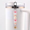 A beaded charm accessory featuring a silver-toned lobster clasp, pink and orange spherical beads, clear faceted beads, small white pearls, a white flower-shaped bead, and a gold-toned metal daisy charm with a yellow center.