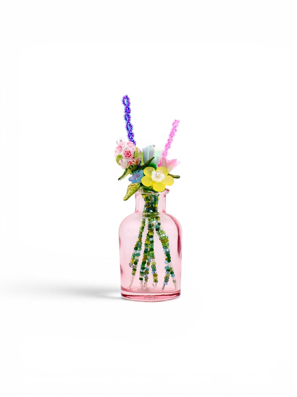 A small, translucent pink glass bottle containing a bouquet of artificial flowers made from colorful beads and wire. The arrangement features yellow, pink, and blue floral shapes with green beaded stems extending into the bottle.