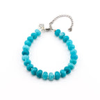 A bracelet featuring round, turquoise-colored beads with varying shades of blue and green. The bracelet includes a silver-toned metal chain extension and a small, rectangular silver charm engraved with the text MADE WITH LOVE.