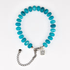 A bracelet composed of round, turquoise-colored beads strung together. The bracelet features a silver-toned metal chain extender and a small, oval-shaped silver-toned metal charm with the text MADE WITH LOVE engraved on the surface.