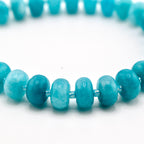 A beaded bracelet featuring smooth, round, turquoise-colored gemstone beads. The beads exhibit natural variations in shade, ranging from light to deep blue-green, and are strung together on a flexible cord, creating a circular shape.