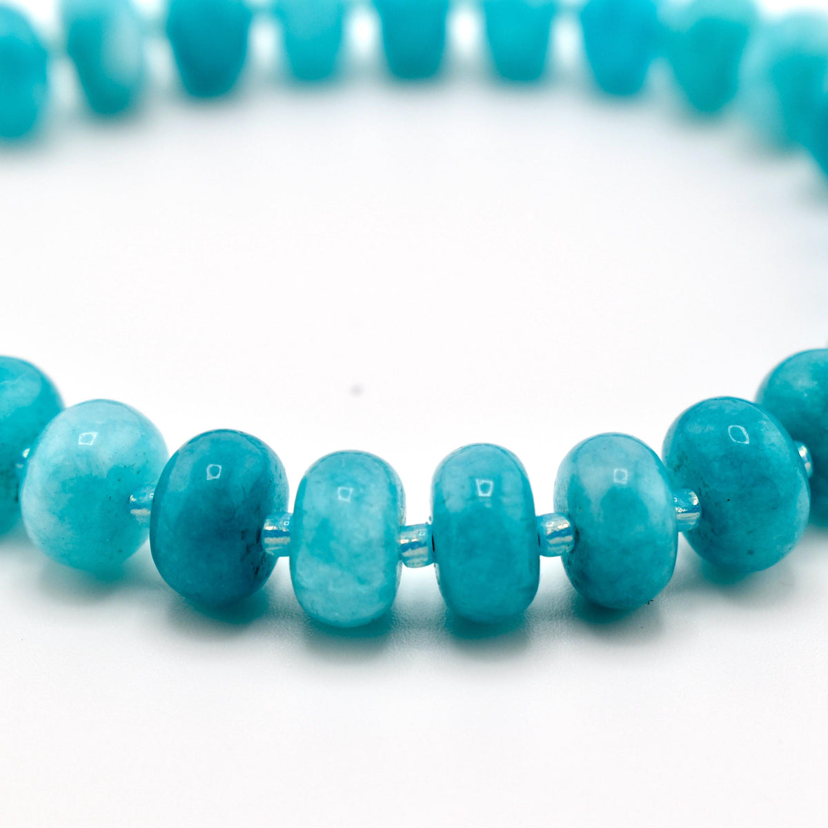 A beaded bracelet featuring smooth, round, turquoise-colored gemstone beads. The beads exhibit natural variations in shade, ranging from light to deep blue-green, and are strung together on a flexible cord, creating a circular shape.