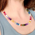 A necklace featuring a single strand of small, smooth, round beads in a vibrant spectrum of colors including red, orange, yellow, green, blue, purple, and white, arranged in a repeating pattern around the neck.