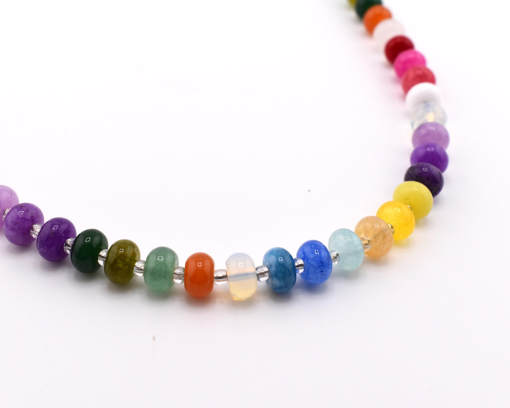 A necklace featuring a single strand of smooth, round, multi-colored beads in shades of purple, green, orange, blue, yellow, and pink, separated by small silver-toned spacers, arranged in a curved line against a plain white background.
