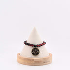 A beaded bracelet featuring alternating translucent red and opaque black spherical beads. A circular bronze-toned metal pendant hangs from the center, displaying an embossed moth design with small crescent moon details on its wings.
