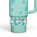 A light teal tumbler featuring a repeating pattern of small dark teal daisies. Wrapped around the lower section is a stack of five beaded bracelets in shades of turquoise, white, and silver, including round, faceted, and flat disc beads.