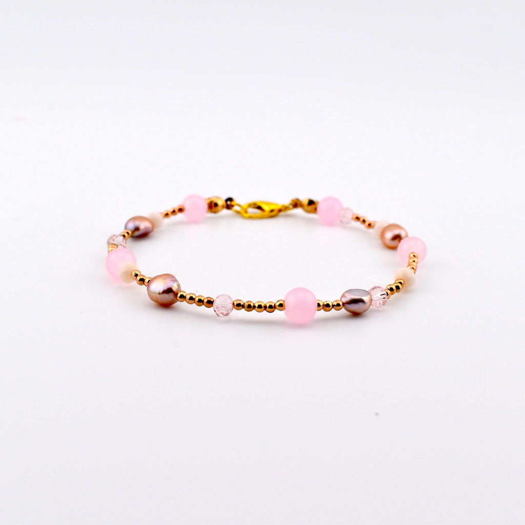 A beaded bracelet featuring a repeating pattern of round pink beads, metallic gold-toned spacer beads, small clear faceted beads, and irregular mauve-toned pearls. The bracelet is secured with a gold-toned lobster claw clasp.