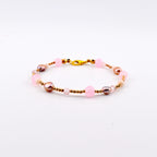 A beaded bracelet featuring a repeating pattern of round pink beads, metallic gold-toned spacer beads, small clear faceted beads, and irregular mauve-toned pearls. The bracelet is secured with a gold-toned lobster claw clasp.