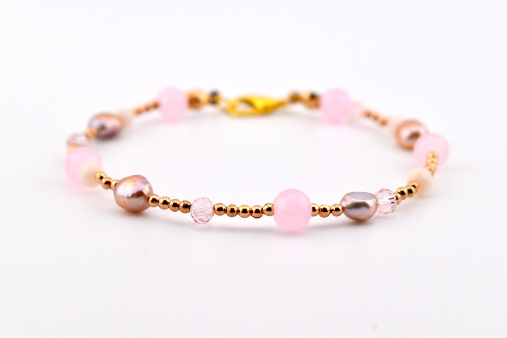 A delicate bracelet featuring a mix of round light pink beads, metallic rose gold-toned spacer beads, and iridescent mauve-colored pearls. The piece is secured with a gold-toned lobster claw clasp, creating a balanced arrangement.