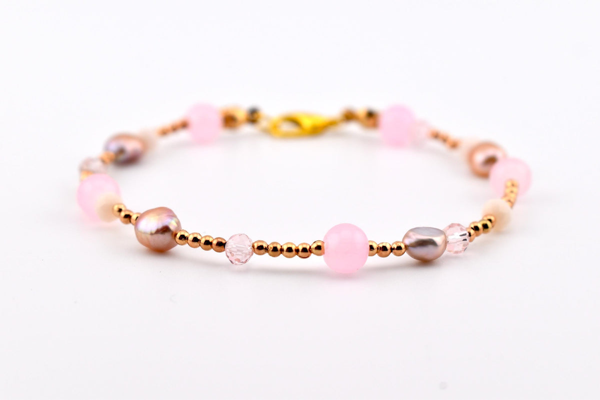 A delicate bracelet featuring a mix of round light pink beads, metallic rose gold-toned spacer beads, and iridescent mauve-colored pearls. The piece is secured with a gold-toned lobster claw clasp, creating a balanced arrangement.
