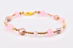 A beaded bracelet featuring a mix of round pink beads, iridescent pearls, small faceted crystals, and tiny metallic gold-tone spacer beads. The bracelet is secured with a gold-tone lobster claw clasp, creating a delicate and layered design.