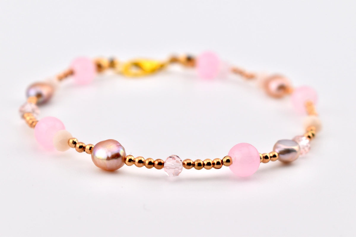 A beaded bracelet featuring a mix of round pink beads, iridescent pearls, small faceted crystals, and tiny metallic gold-tone spacer beads. The bracelet is secured with a gold-tone lobster claw clasp, creating a delicate and layered design.