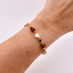 A beaded bracelet featuring a mix of small gold-toned metallic beads, white irregular freshwater pearls, and translucent brown glass beads. The beads are arranged in a repeating pattern along a thin, flexible cord worn around the wrist.
