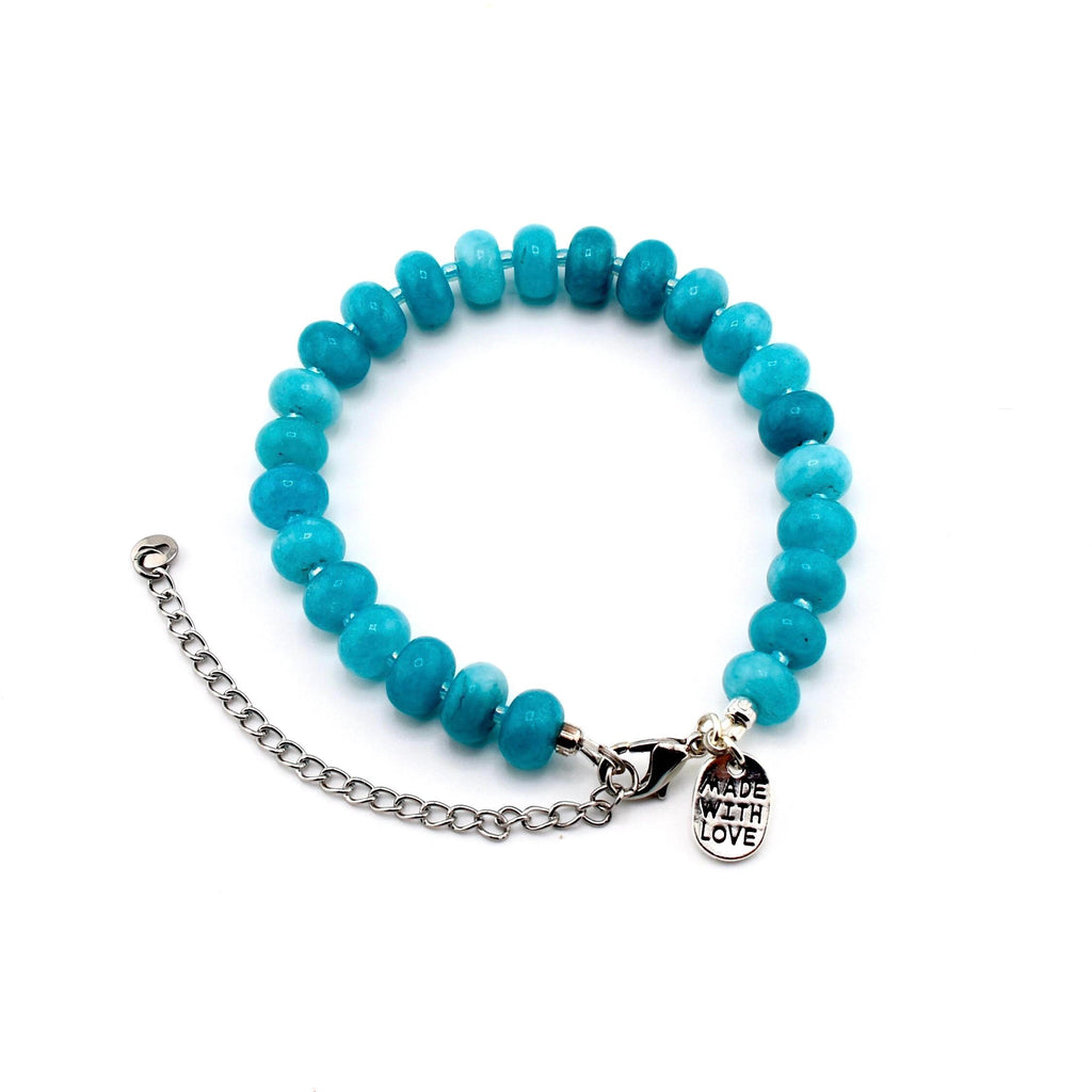 A bracelet featuring round, turquoise-colored beads strung together. It includes a silver-toned metal chain extender and a lobster claw clasp. A small, oval-shaped silver metal charm is attached, engraved with the text MADE WITH LOVE.