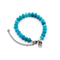 A bracelet featuring round, turquoise-colored beads strung together. It includes a silver-toned metal chain extender and a lobster claw clasp. A small, oval-shaped silver metal charm is attached, engraved with the text MADE WITH LOVE.