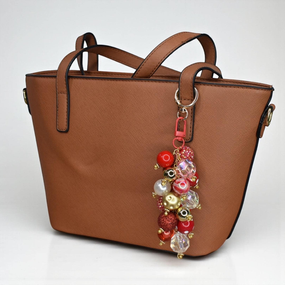 A brown handbag with a beaded keychain. The keychain features a cluster of red, gold, and clear beads. The handbag has two handles and a shoulder strap.