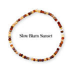 A circular beaded bracelet featuring a variety of small glass beads in shades of brown, tan, gold, and clear. The text "Slow Blurn Sunset" is printed in the center of the circular arrangement of beads against a plain white background.
