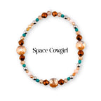 A circular beaded bracelet featuring a mix of faceted copper-toned, smooth turquoise, metallic silver, and pale peach beads. The text Space Cowgirl is printed in black in the center of the circular arrangement of the beaded jewelry.
