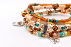 A multi-strand beaded bracelet featuring amber, brown, and turquoise glass beads, beige disc spacers, and silver-toned metal charms shaped like a cowboy hat, a cowboy boot, and a horse head, all strung on a flexible elastic cord.