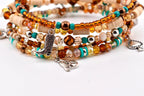 A multi-strand bracelet set featuring a mix of amber, brown, and turquoise beads, along with flat beige disc beads. The bracelet includes silver-toned metal charms shaped like a cowboy boot, a horse head, and a spade playing card.