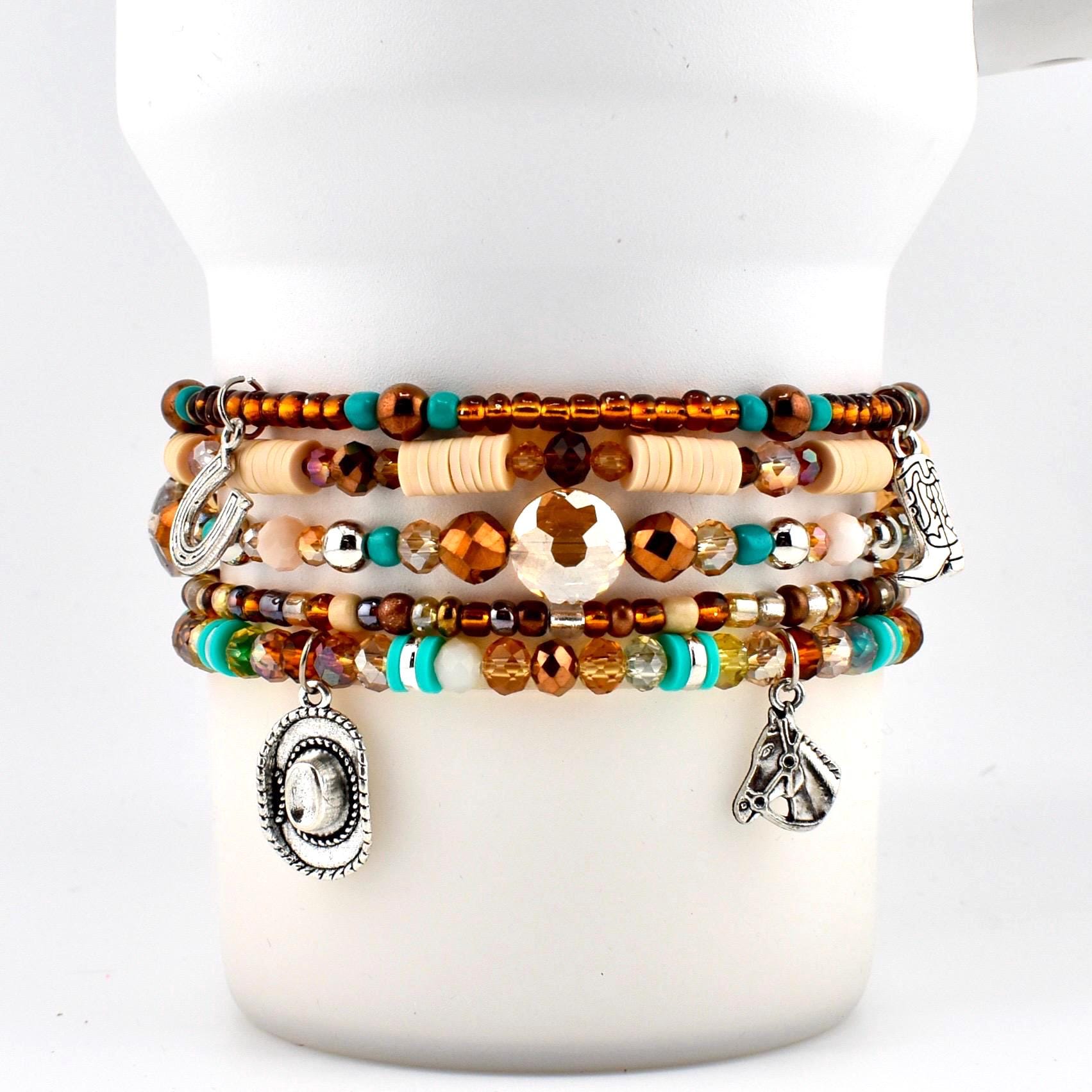 A multi-strand beaded bracelet featuring brown, turquoise, and cream-colored beads. The bracelet includes silver-toned charms shaped like a horseshoe, a cowboy hat, a cowboy boot, and a horse head, interspersed with faceted crystals.