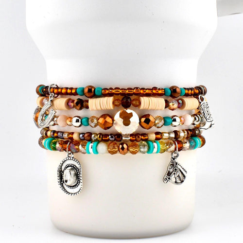 A multi-strand beaded bracelet featuring brown, turquoise, and cream-colored beads. The bracelet includes silver-toned charms shaped like a horseshoe, a cowboy hat, a cowboy boot, and a horse head, interspersed with faceted crystals.