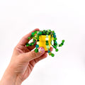 A miniature yellow ceramic pot containing a decorative plant made of various green and translucent beads. The beaded strands hang over the rim of the pot, featuring different shades of green, lime, and teal glass beads in assorted sizes.