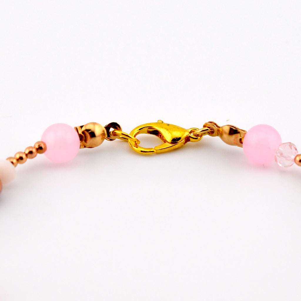 A gold-toned lobster claw clasp connects two segments of a beaded bracelet. The bracelet features smooth, round, light pink beads, smaller metallic gold-toned spherical beads, and a single clear faceted bead on the right side.
