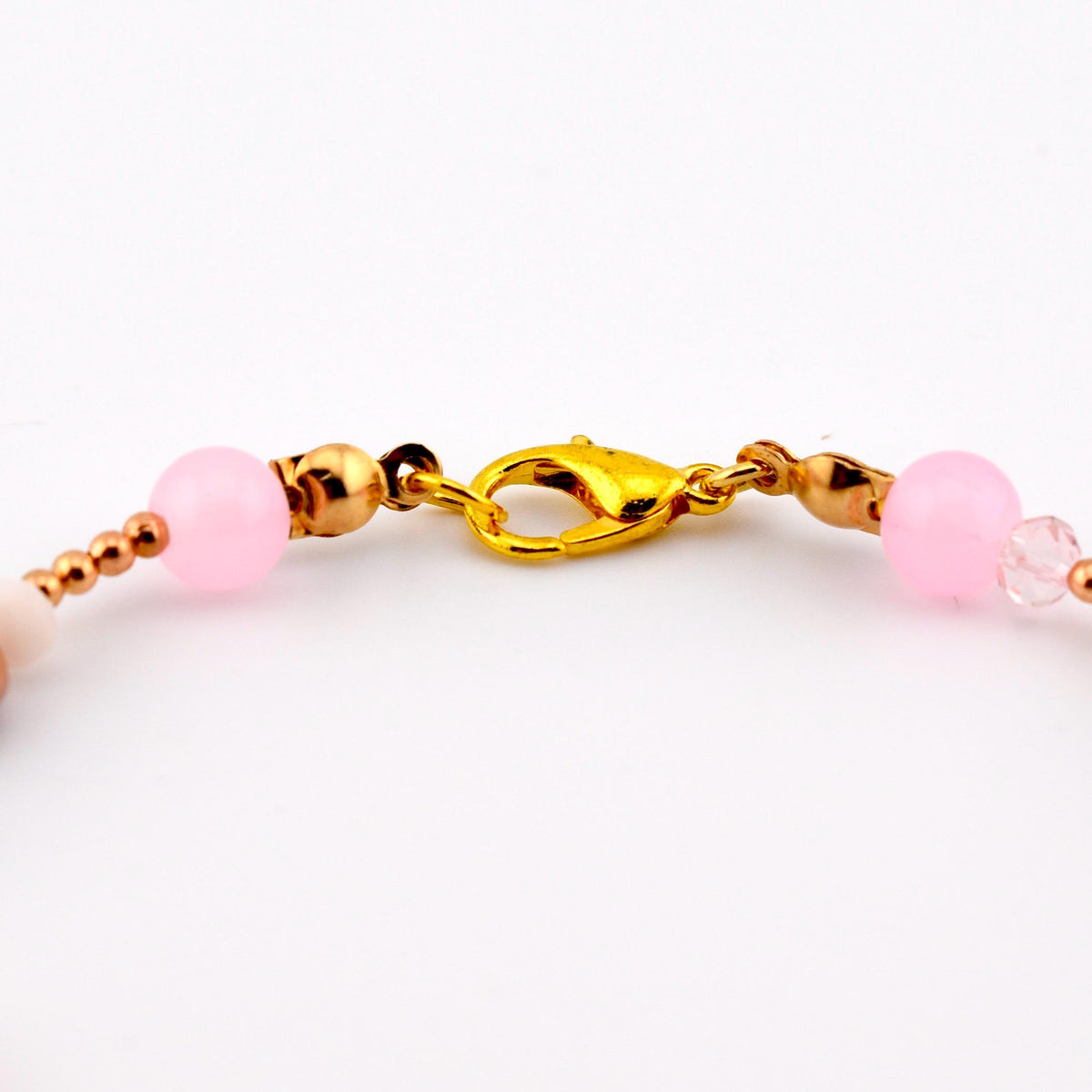 A gold-toned lobster claw clasp connects two segments of a beaded bracelet. The bracelet features smooth, round, light pink beads, smaller metallic gold-toned spherical beads, and a single clear faceted bead on the right side.