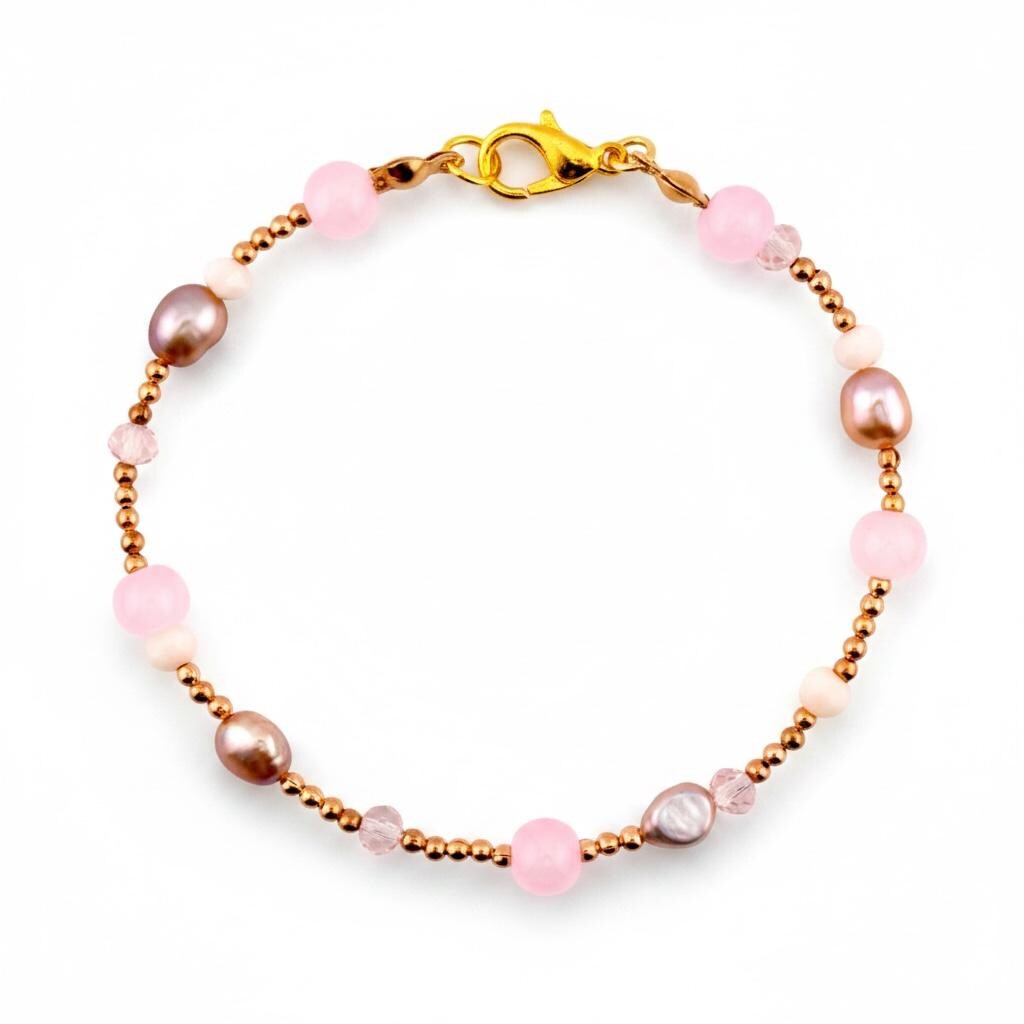 A delicate bracelet featuring a gold-toned chain interspersed with smooth pink spherical beads, small off-white beads, and irregular brown oval-shaped pearls. The piece is secured with a gold-toned lobster claw clasp closure.