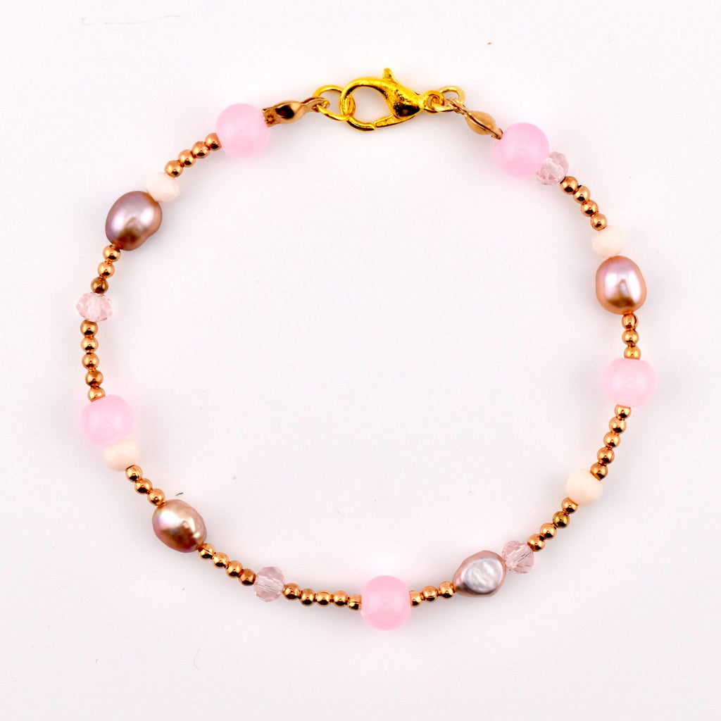 A beaded bracelet featuring a gold-tone lobster claw clasp, alternating between small metallic gold beads, smooth pink spherical beads, off-white round beads, faceted clear crystals, and irregular iridescent mauve-toned pearls.