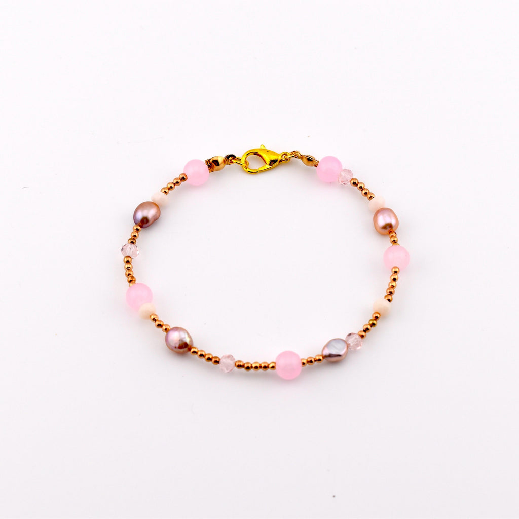 A beaded bracelet featuring a gold-tone lobster claw clasp, alternating between small metallic gold beads, round translucent pink beads, and irregular-shaped iridescent brown pearls, arranged in a circular pattern on a white background.